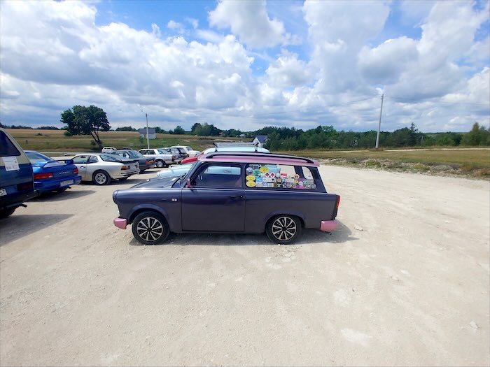 Fioletowy Trabant kombi z różowymi zderzakami na żwirowym parkingu