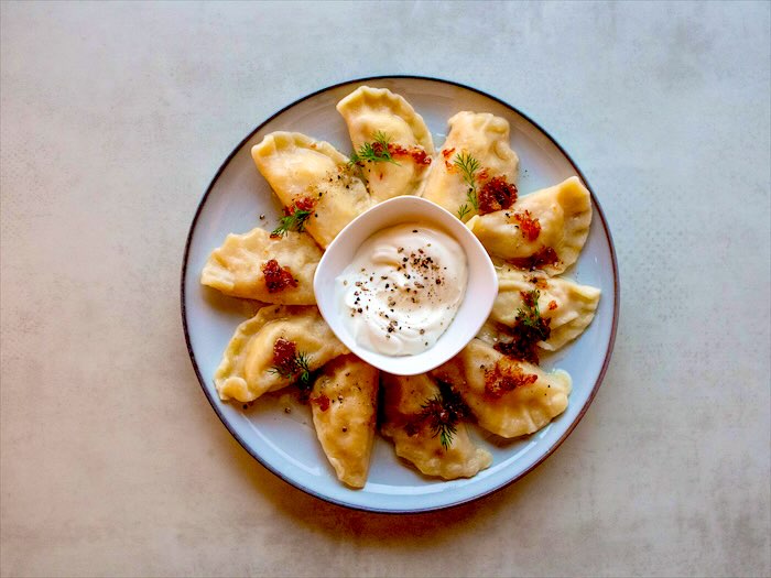Pierogi ze skwarkami, koperkiem i miseczką śmietany na talerzu