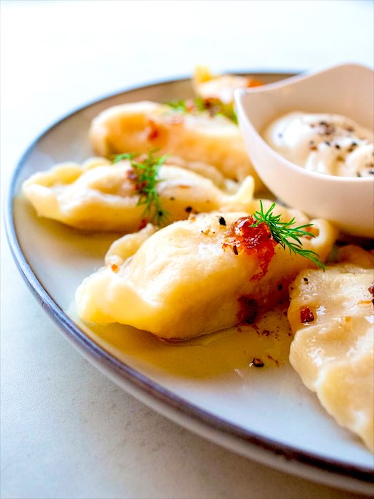 Pierogi polane masłem ze skwarkami i koperkiem, obok śmietana