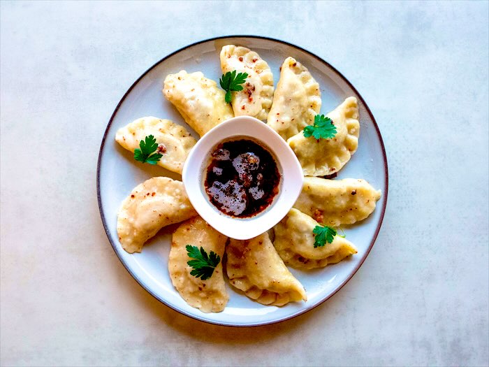 Pierogi z natką pietruszki i ciemnym sosem w miseczce