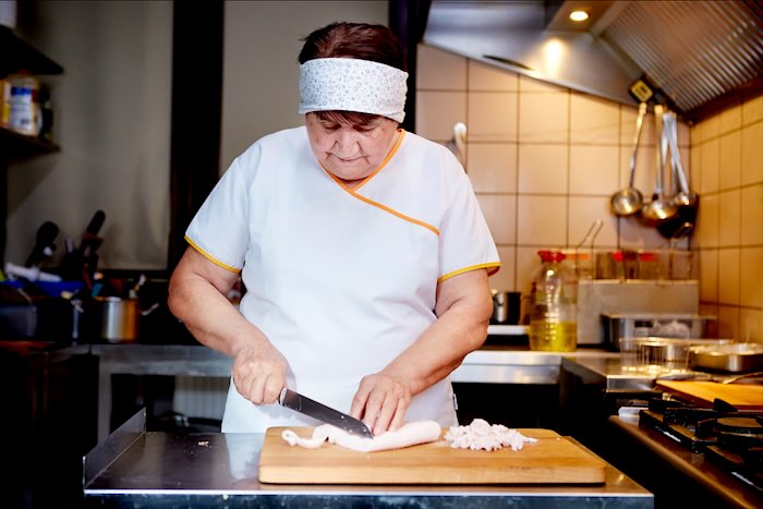 Kucharka kroi mięso na drewnianej desce w kuchni