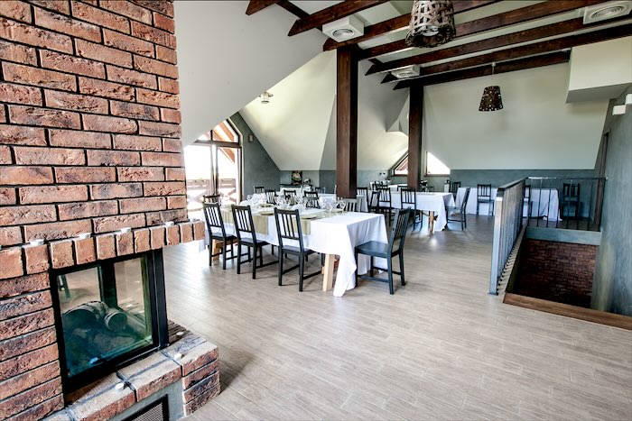 Sala Kominkowa z przeszklonym kominkiem, drewnianymi belkami i nakrytymi stołami
