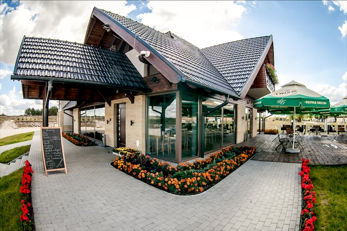 Zajazd od frontu z tablicą menu, klombami kwiatów i tarasem